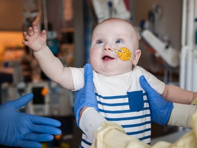 A smiling baby being held up by a person in medical attire